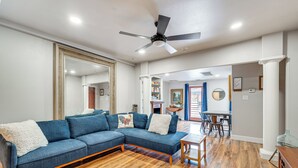 Una sala de estar con un sofá modular, piso de madera, ventilador de techo y un comedor con sillas y mesa.