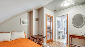 Un dormitorio con una cama, una mesita de noche de madera, un aparador y una puerta que da a un baño.