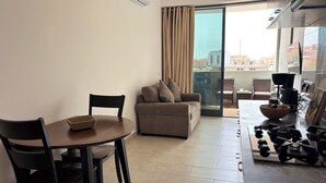 Un salon moderne comprenant un canapé, une table à manger avec des chaises, un coin cuisine avec une machine à café et un balcon avec des rideaux.