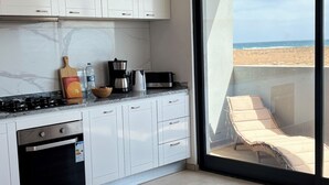 A modern kitchen with white cabinets, a gas stove, and a view of a beach through a large sliding glass door. - Joli Beach House - Third floor T3 Apartment with beautiful Views (Santa Maria)
