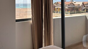 A room with a large window, a bed, and a view of a beach and buildings. - Joli Beach House - Third floor T3 Apartment with beautiful Views (Santa Maria)