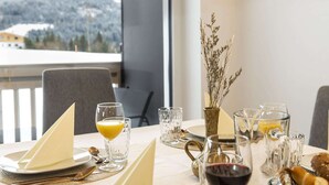 Une table à manger dressée avec une serviette, un verre de jus d’orange, un verre à vin et un petit vase contenant des fleurs séchées.