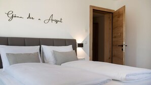 Un lit bien fait, avec du linge de lit blanc et deux oreillers, une porte en bois sur la droite et un mur sur lequel est affiché un panneau indiquant : « Offrez-vous un moment de détente ».