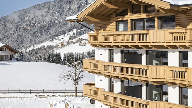 Un chalet en bois à plusieurs étages, doté de balcons, qui se dresse sur fond de montagnes enneigées.