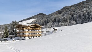 Un bâtiment en bois à plusieurs étages, doté de balcons, entouré d’arbres couverts de neige et avec une montagne en arrière-plan.