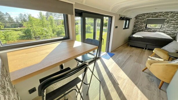 Indretning i en kompakt, moderne autocamper med spiseplads, seng og stort vindue med en smuk udsigt.