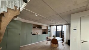 Eine moderne Küche mit grünen Schränken, eine Essecke mit rundem Tisch und Stühlen sowie eine Treppe mit Holzstufen.