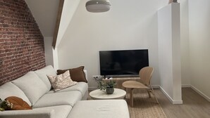 Ein modernes Wohnzimmer mit Backsteinwand, Flachbildfernseher, Sofa, Couchtisch und Sessel.