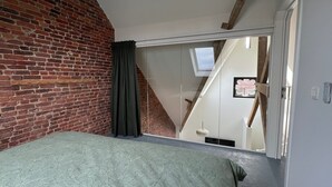 Ein Schlafzimmer mit Backsteinwand, einem Bett mit gemustertem Überwurf, einem Oberlicht und einer Treppe zu einer oberen Etage.