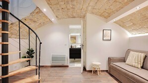 Een modern interieur met een spiltrap, een stenen plafond, een bank en een klein krukje.