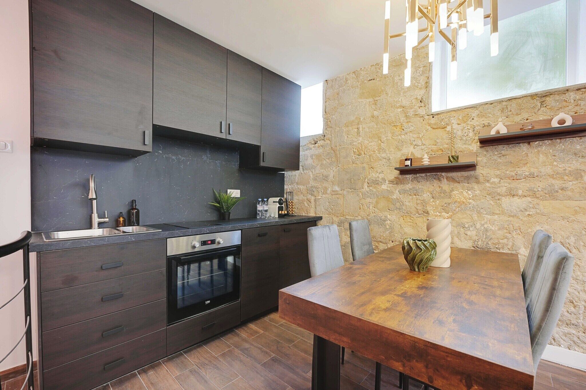 A modern kitchen with dark cabinetry, a built-in oven, and a dining area with a wooden table and chairs.