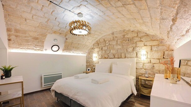 Een slaapkamer met een stenen plafond, een bed met witte lakens, een nachtkastje met een lamp en een radiator.