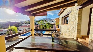A terrace with a stone wall, a pool, and a table with chairs. - Charming villa with private garden (Alfaz del Pi)