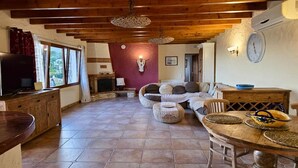 A cozy living room with a wooden ceiling, a television, a sofa, and a dining area with a wooden table and chairs. - Charming villa with private garden (Alfaz del Pi)