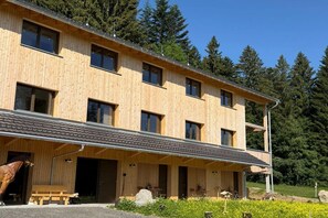 A wooden building with multiple windows and a covered entrance area. - Dog-friendly holiday apartment in Bregenzerwald (Sibratsgfäll)