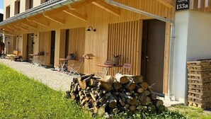 Een houten gebouw met een overdekte veranda, buitenmeubels en een stapel hout voor de kachel.