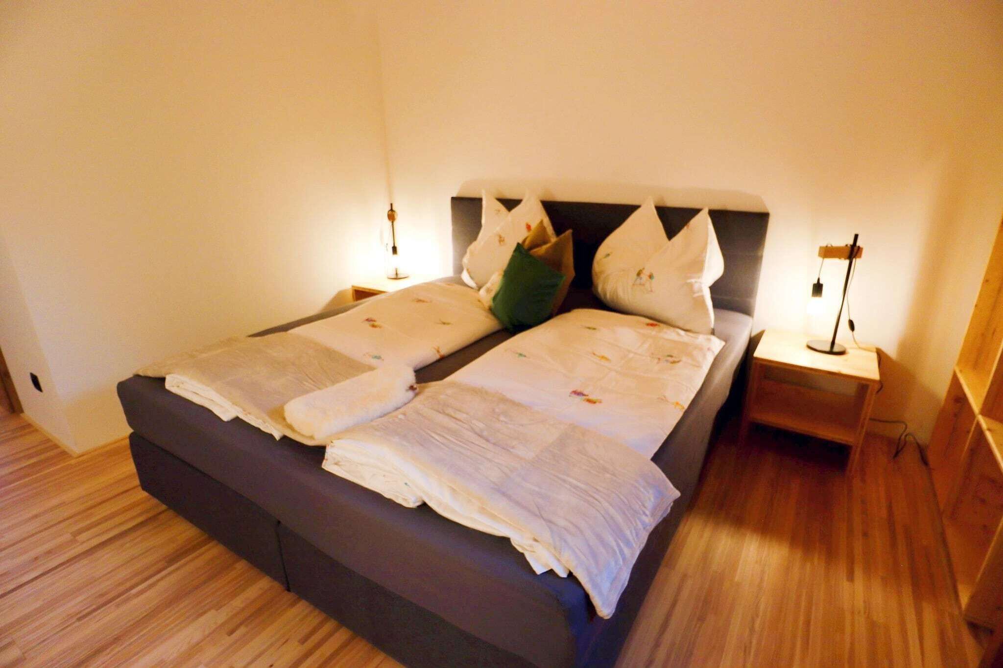 Una cama bien hecha con un cabecero oscuro, dos mesitas de noche con lámparas y suelo de madera.