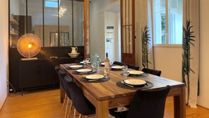 Ein Essbereich mit einem Holztisch, gedeckt für sechs Personen, einem modernen Kronleuchter und Blick in die Küche durch eine Glastür.
