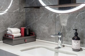 A modern bathroom with a marble wall, a white sink, a mirror, and a towel rack with folded towels and a red cup. - ECHENG Hotel Bayi Square Nanchang (Nanchang)