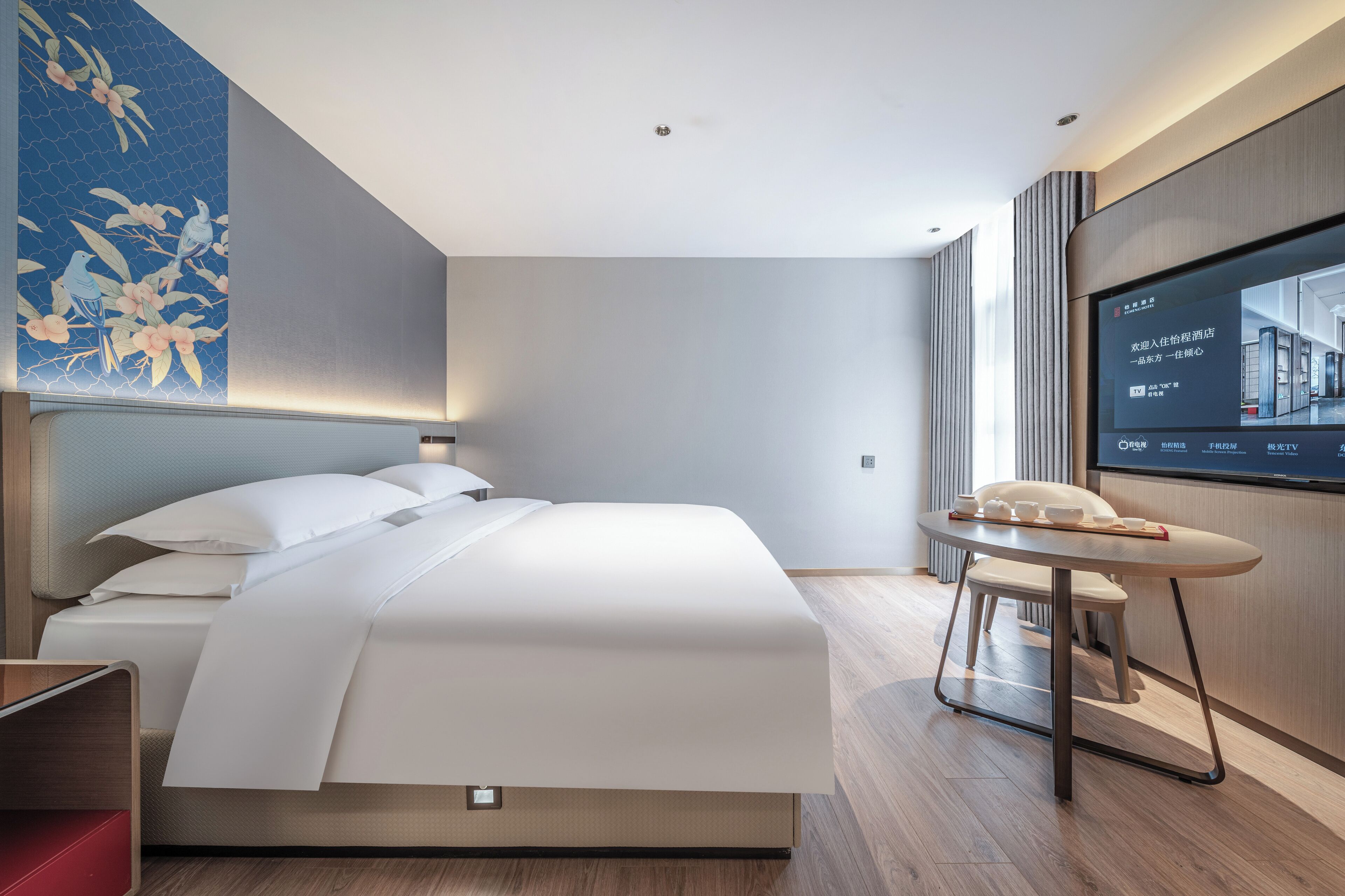 A modern hotel room with a large bed, a bedside table, a TV, and a wall with a floral mural.