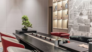 Een moderne eetruimte met een lange tafel, rode en witte stoelen, een bonsai en een muur met een stadsgezicht.