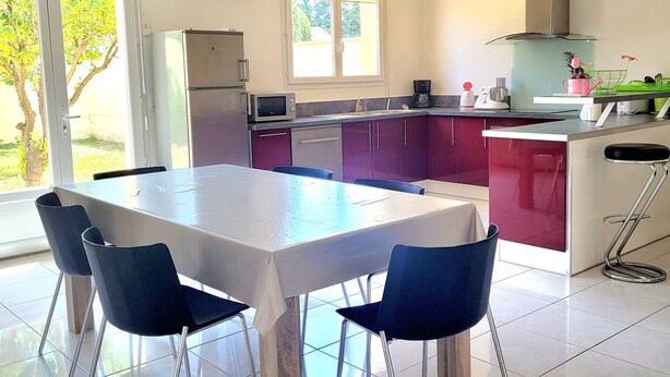 Eine moderne Küche mit Essbereich, ausgestattet mit einem großen Tisch, Stühlen und Blick ins Freie.