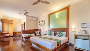 A hotel room with a large bed, a desk, a chair, a ceiling fan, and a small kitchenette. - Treebo Akshaya Palace Inn (Mysore)