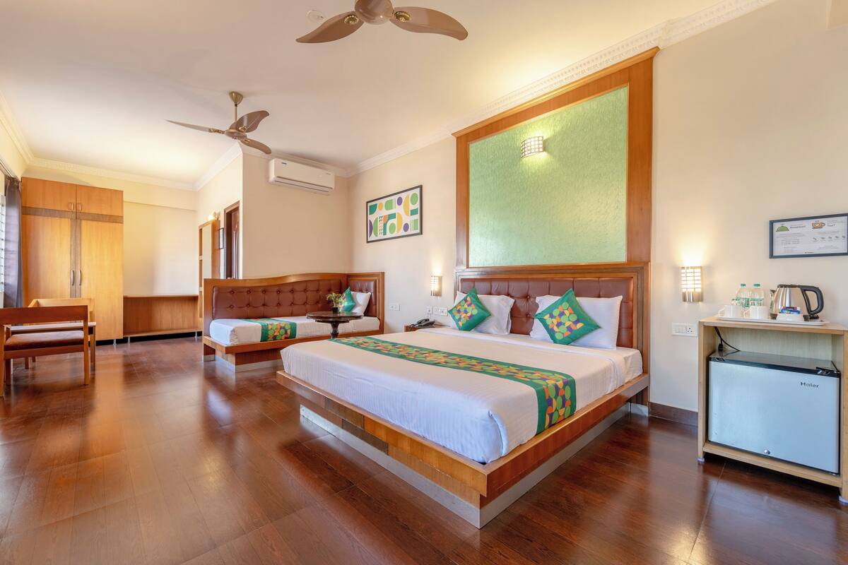 A hotel room with a large bed, a desk, a chair, a ceiling fan, and a small kitchenette.