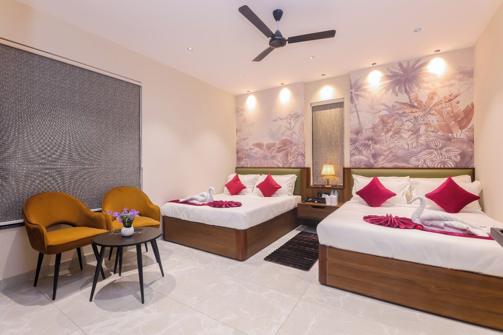 A hotel room with two beds, a sofa, a small table, and a ceiling fan.