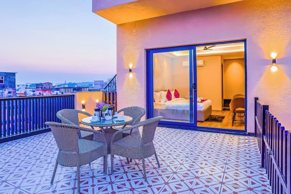 Ein Balkon mit Tisch und Stühlen, ein Bett mit roten Kissen und Blick auf die Stadt.
