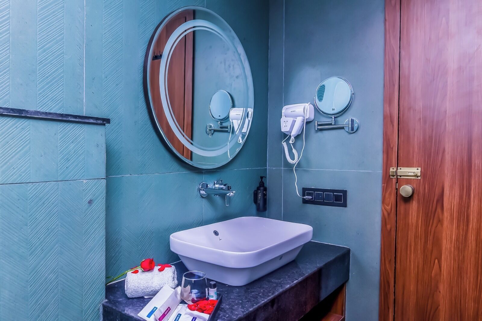 Une salle de bain avec un lavabo blanc, un miroir, un sèche-cheveux et une porte en bois.