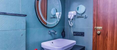 Une salle de bain avec un lavabo blanc, un miroir, un sèche-cheveux et une porte en bois.
