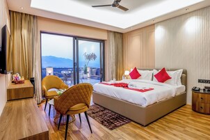 Quarto de hotel com uma cama grande, uma escrivaninha, uma cadeira e uma varanda com vista.