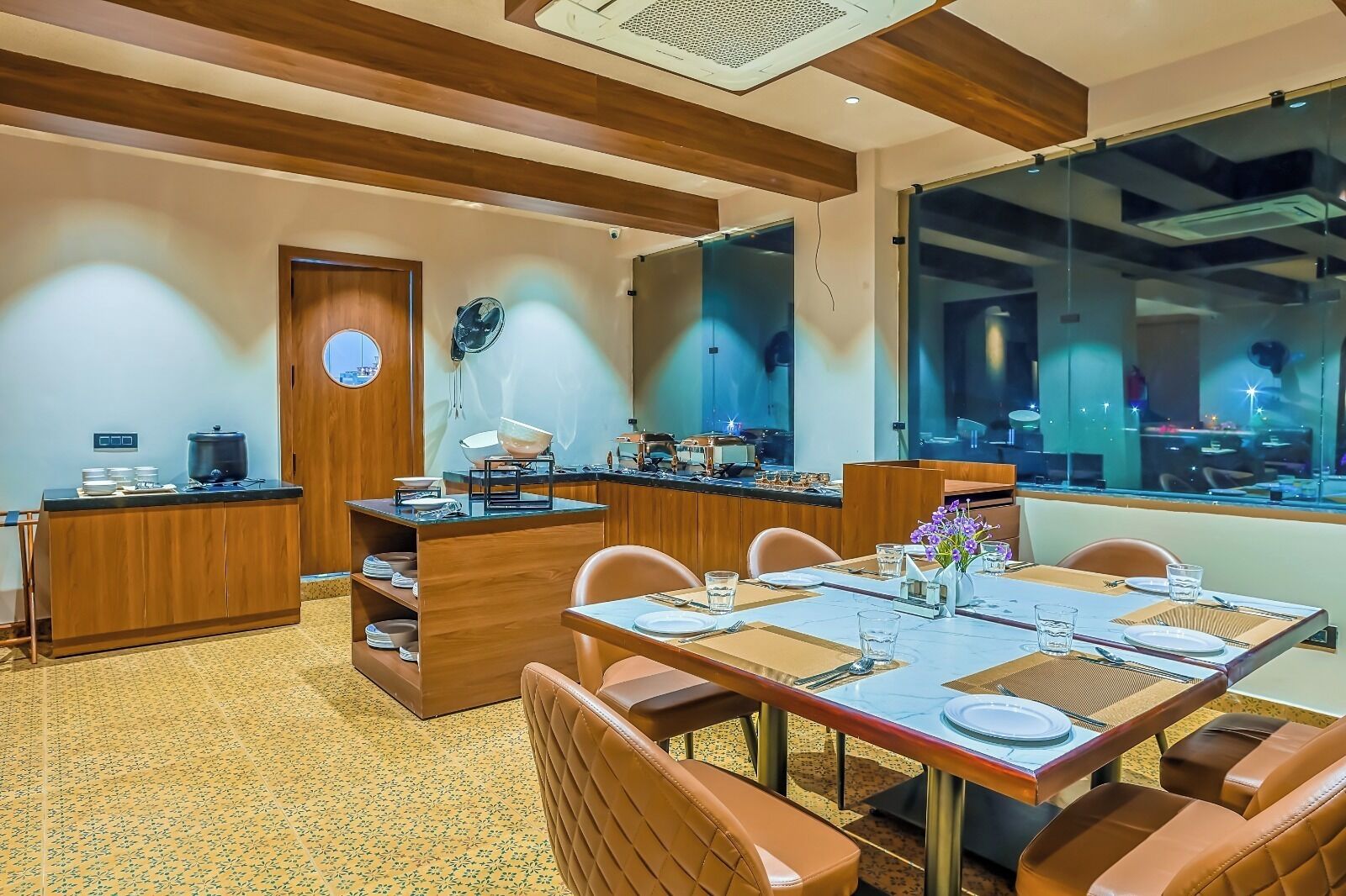 A modern dining area with a wooden counter, a buffet setup, and a large window offering a view of the cityscape.