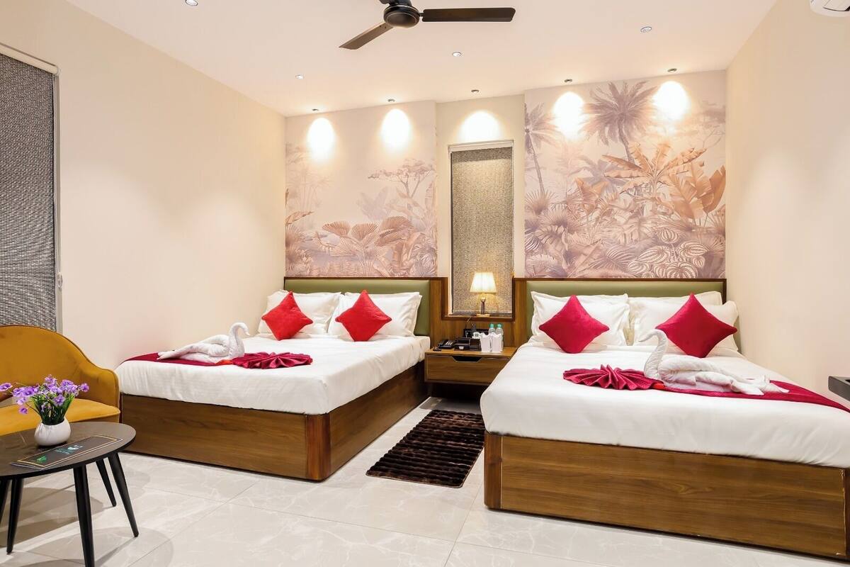 Ein Hotelzimmer mit zwei Betten, einem kleinen Tisch mit Blumen in einer Vase, einem Deckenventilator und einer Wand mit einem tropischen Wandgemälde.