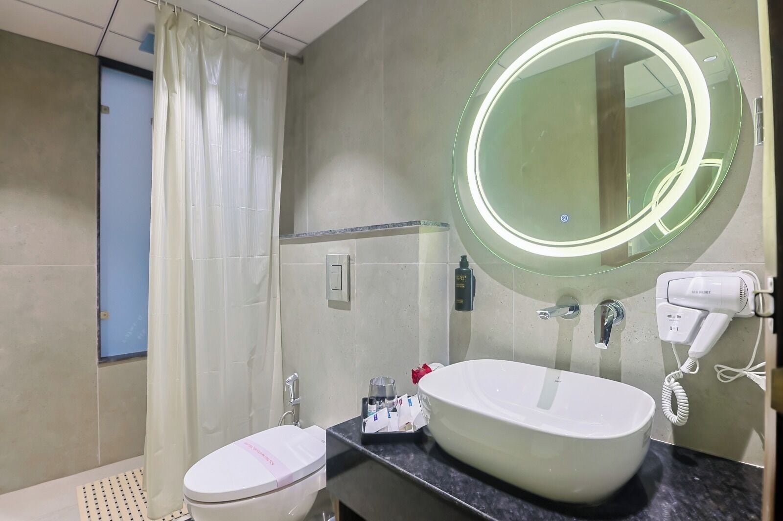 A modern bathroom with a toilet, sink, and a large mirror with a light.