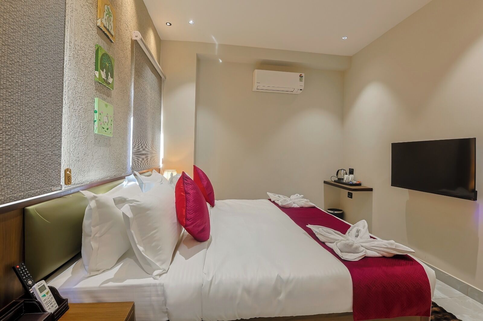 A hotel room with a bed, a TV, a desk with a phone, and a wall-mounted air conditioner.