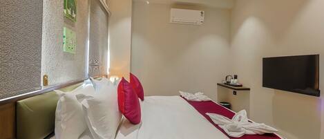 A hotel room with a bed, a TV, a desk with a phone, and a wall-mounted air conditioner.