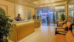 A hotel reception area with a receptionist, a reception desk, a seating area with orange patterned sofas, and a chandelier. - Arina Vedic Haveli 2 Min walk to Ganga (Haridwar)