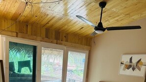 Ein Schlafzimmer mit einem hölzernen Kopfteil, einem Bett mit weißer Bettwäsche, einem Deckenventilator und einem großen Fenster mit Blick auf Grünflächen.