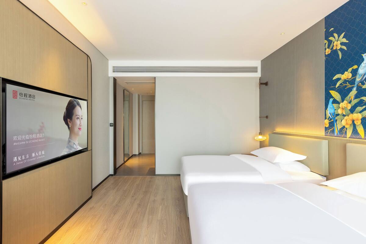 A hotel room with a bed, a TV mounted on the wall, and a painting on the wall.