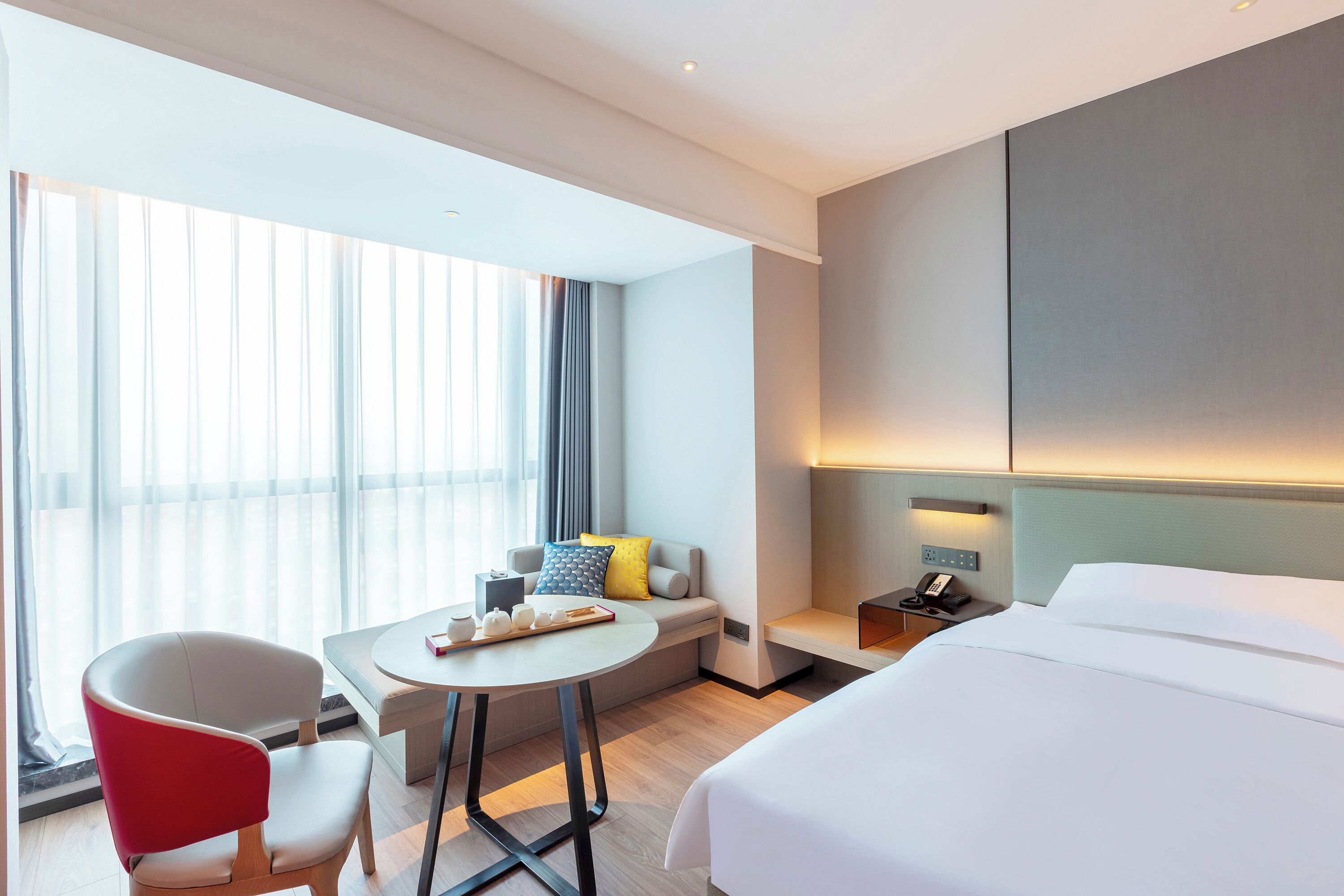 Une chambre d’hôtel moderne équipée d’un lit, d’un bureau, d’une chaise, d’un canapé et d’une fenêtre avec des rideaux.