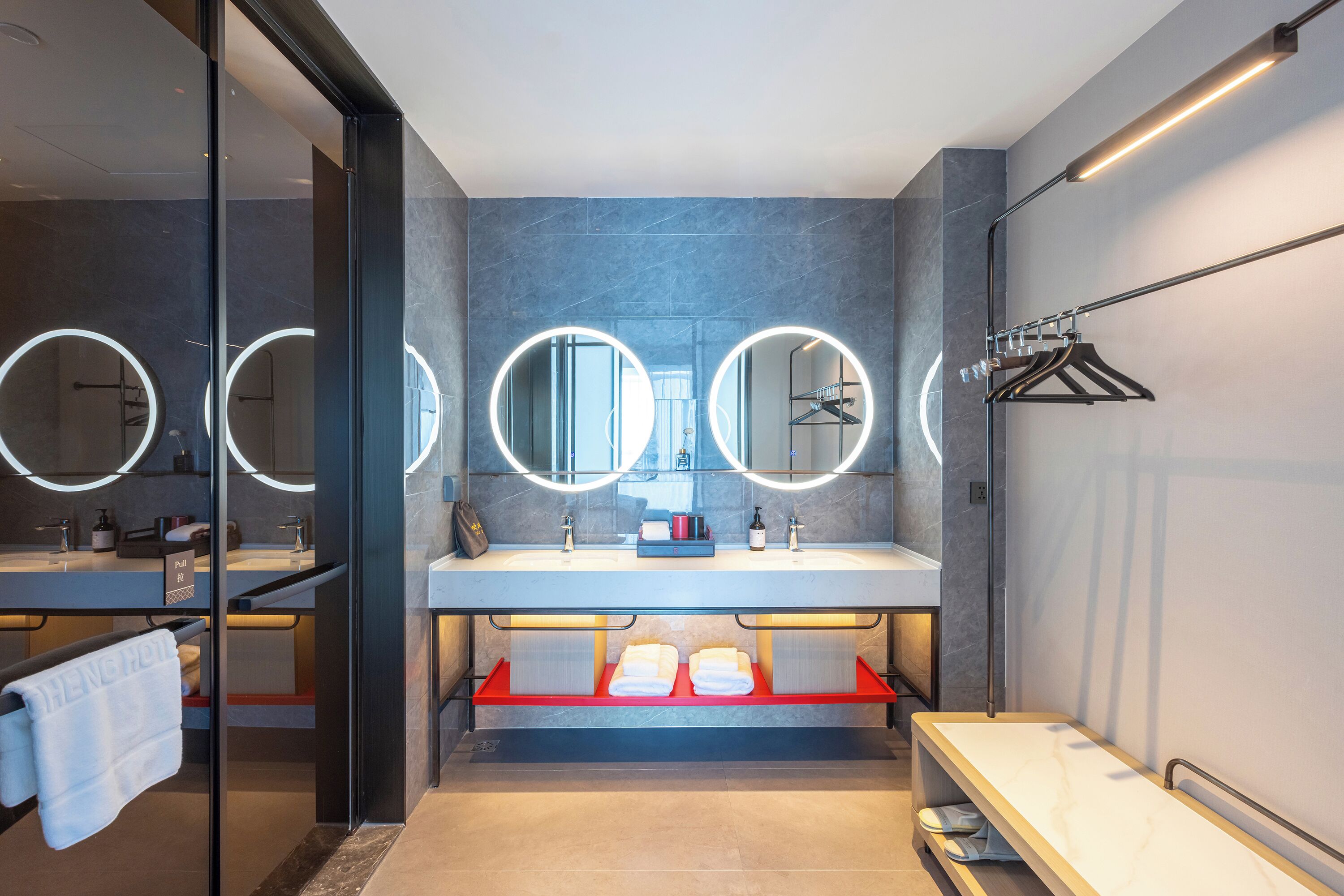 Un baño moderno con dos lavamanos, espejos redondos y un perchero para toallas.