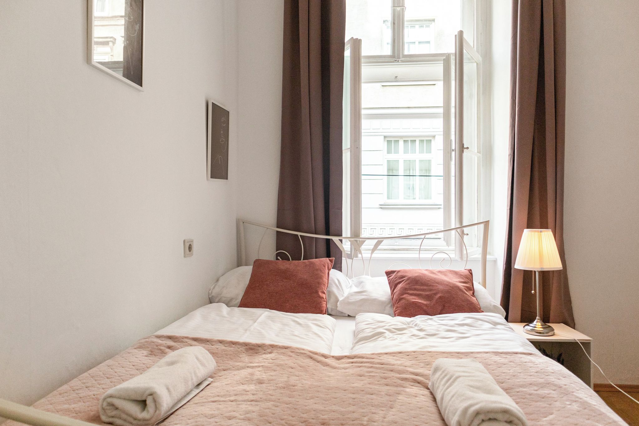 Una cama bien hecha con dos almohadas, una lámpara de noche y una ventana con cortinas.