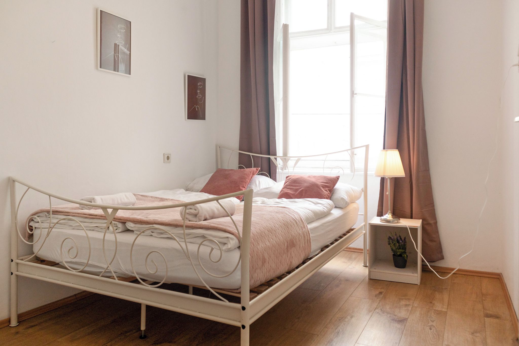 A single-bed room with a metal frame, a bedside table with a lamp, and a potted plant.