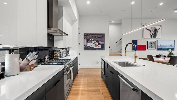 Una cocina moderna con una isla central, un área de comedor con mesa y sillas, y una escalera que conduce a un nivel superior.