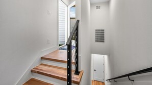 Una escalera de madera con barandilla negra que conduce a una puerta con respiradero.