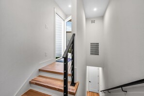 En trappa med trästeg och ett svart räcke, som leder upp till en dörr med ett ventilationsgaller.