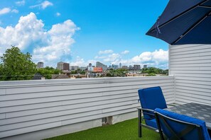 A rooftop terrace with a view of a city skyline, a table with chairs, and a blue awning.