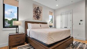Un dormitorio con cama, mesitas de noche, una ventana y una puerta.
